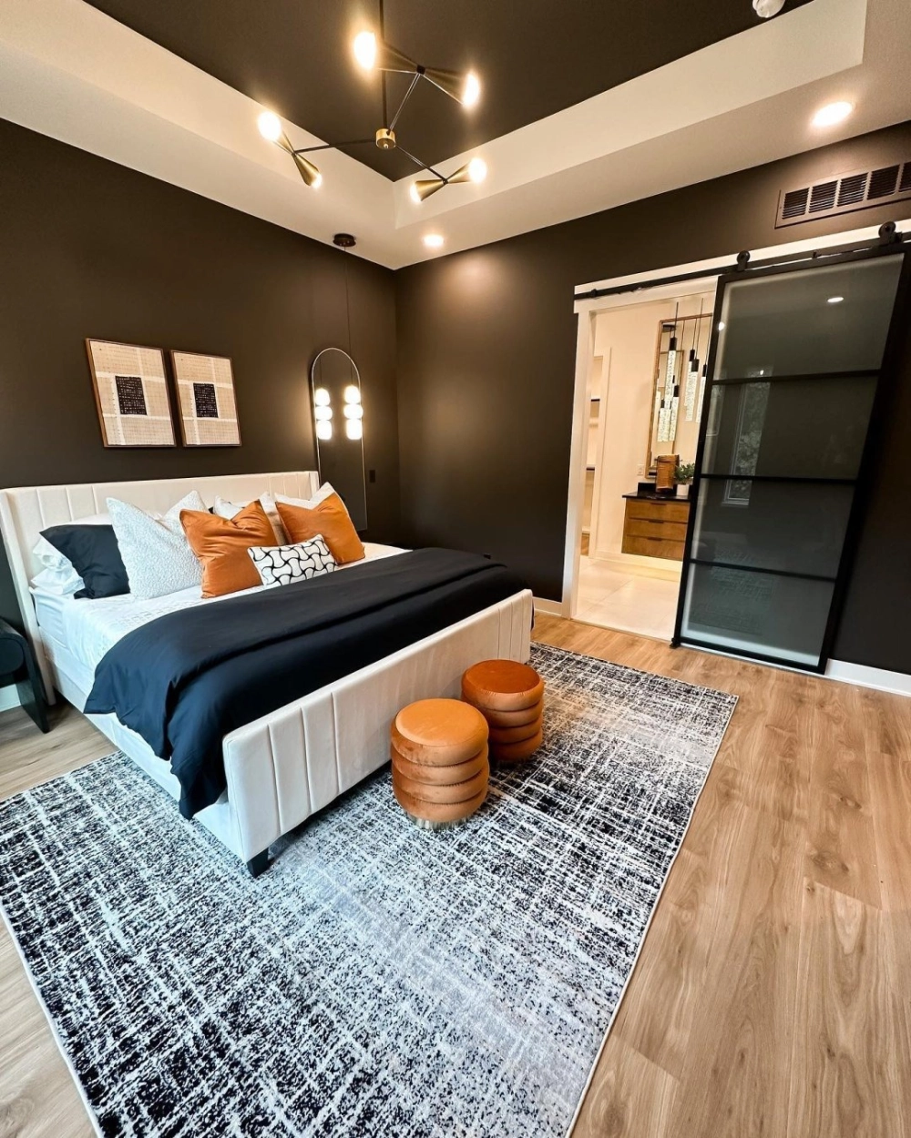 Thiết kế nội thất hiện đại với màu sơn phòng ngủ tông nâu socola làm nền cho giường ngủ màu trắng và gối tựa cam nổi bật